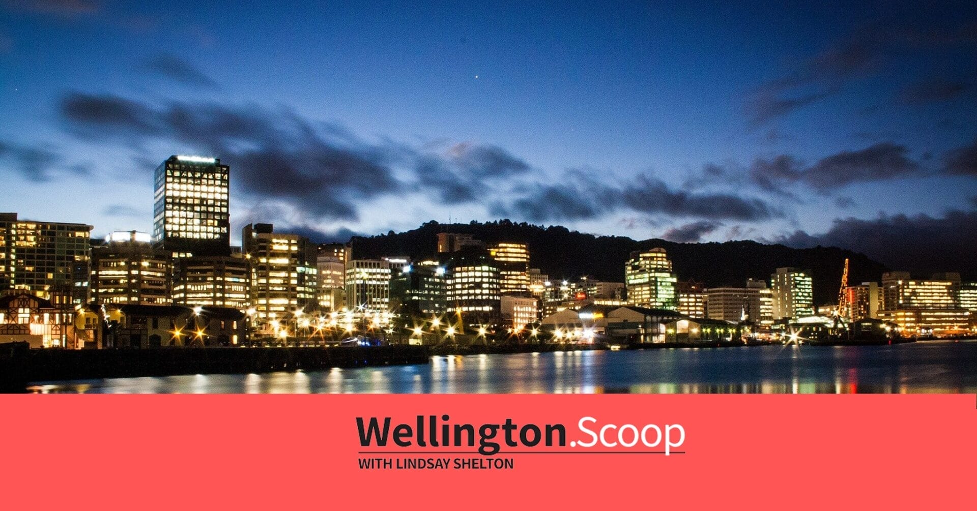 A view of Wellington city’s skyline at dusk, with illuminated buildings reflecting on the waterfront. The sky is deep blue with scattered clouds. A red banner at the bottom reads “Wellington Scoop with Lindsay Shelton.”.