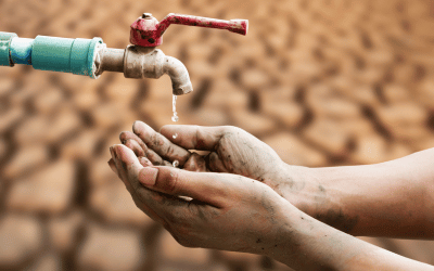 A pair of dirty hands are held under a dripping faucet, with only a few drops of water falling, set against a background of dry, cracked earth, symbolizing water scarcity and drought.