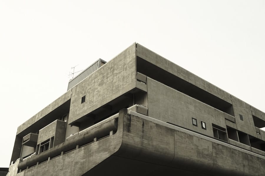A low-angle view of a large, brutalist concrete building with angular shapes and minimal windows, set against a pale, overcast sky.