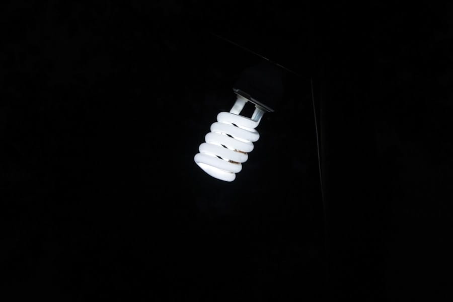 A glowing spiral-shaped compact fluorescent light bulb is illuminated in the darkness, with its bright white light standing out against a black background.